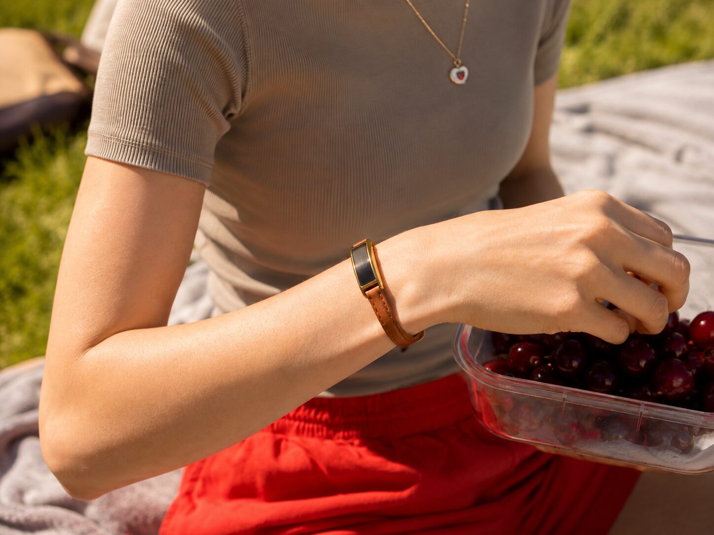 A woman wearing Ray in Sunlit Gold and Cognac Leather reaches into a tub of cherries at a sunny picnic